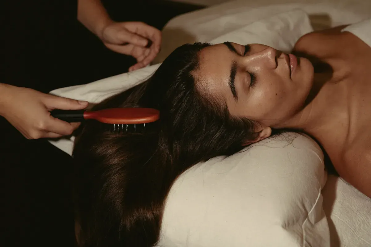 A brush gliding through a relaxed client's hair on a spa bed