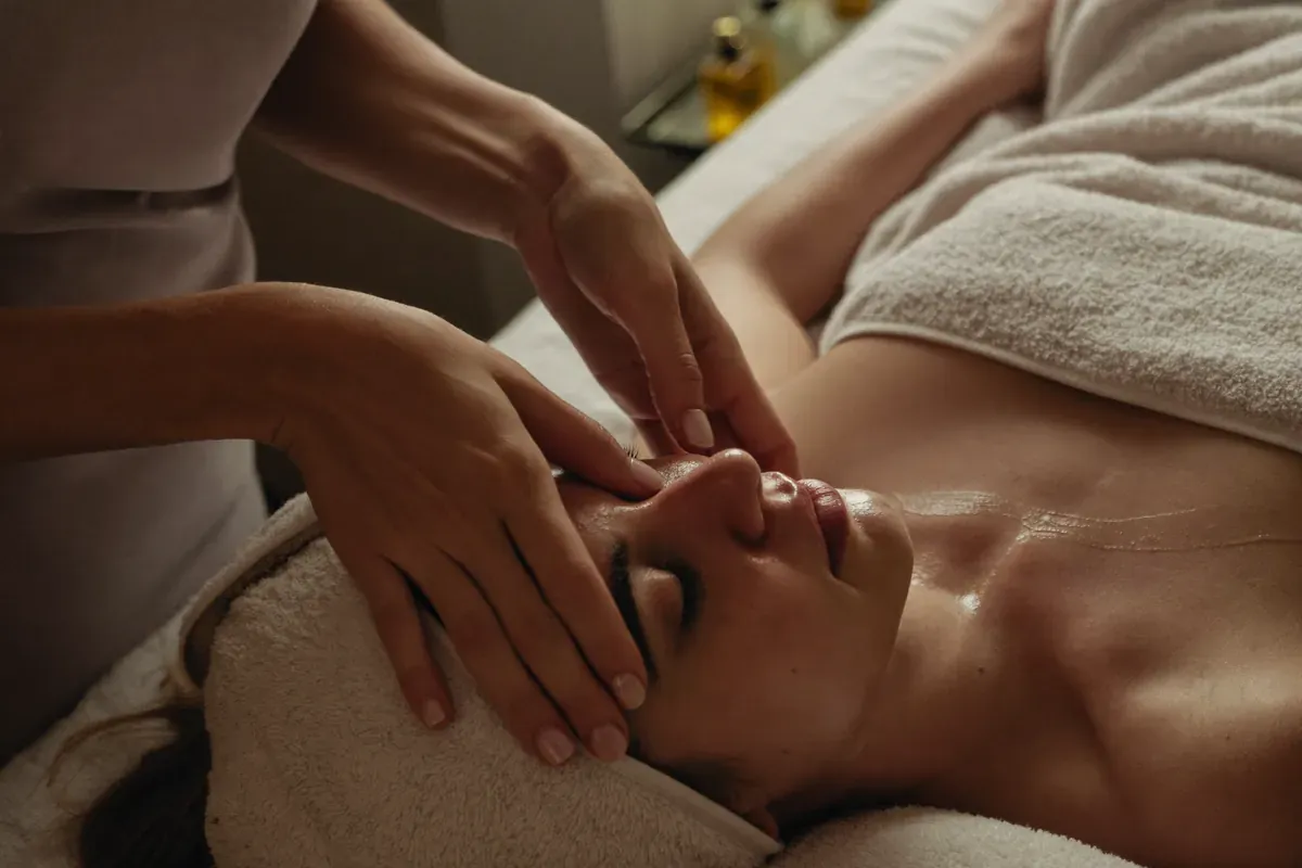 An esthetician's hands massaging a relaxed client's cheeks during a facial