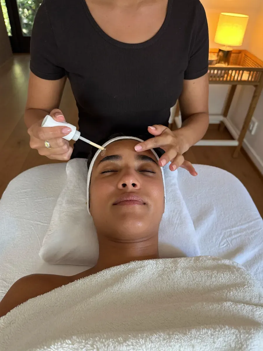Serum being dropped onto a client's forehead from a dropper bottle during a facial